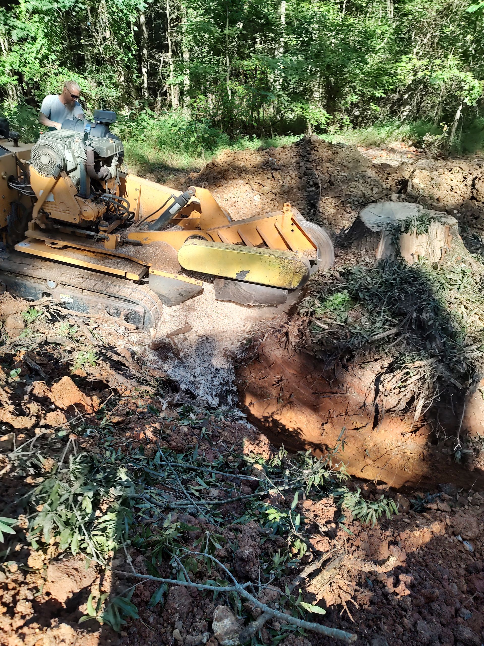 Bulldozer clearing a muddy dirt path in a wooded area