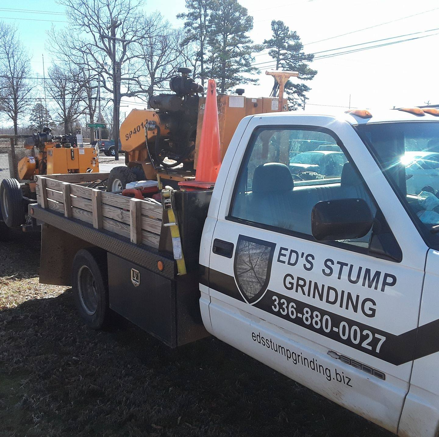 Ed's Stump Grinding truck with a stump grinder on a trailer, parked on a roadside.