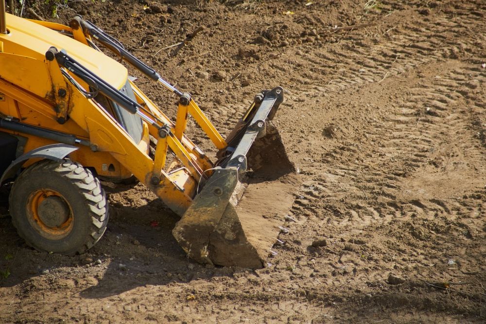 Yellow backhoe digging in dirt, leaving tire tracks.