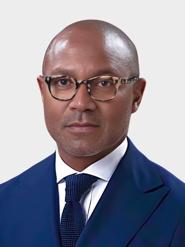 Portrait of a man in a blue suit, white shirt, and glasses against a light background