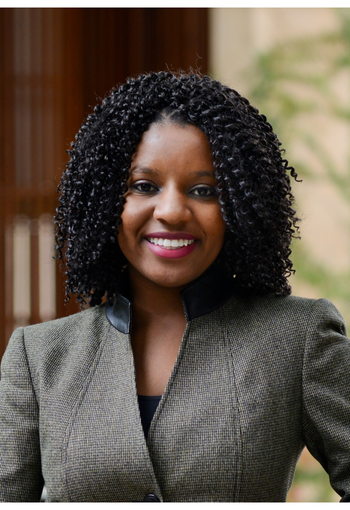 Smiling woman in a gray blazer against a blurred indoor background