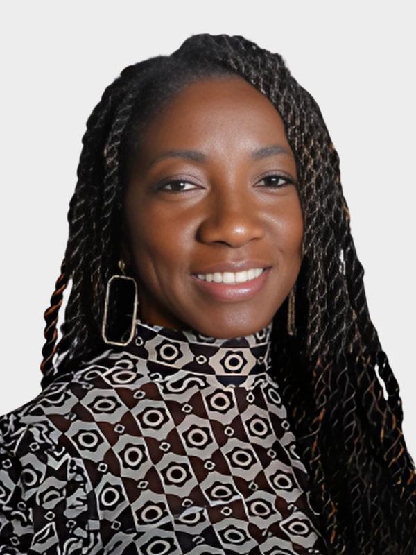 Woman smiling in a patterned black-and-white top with long braided hair and large rectangular earrings.
