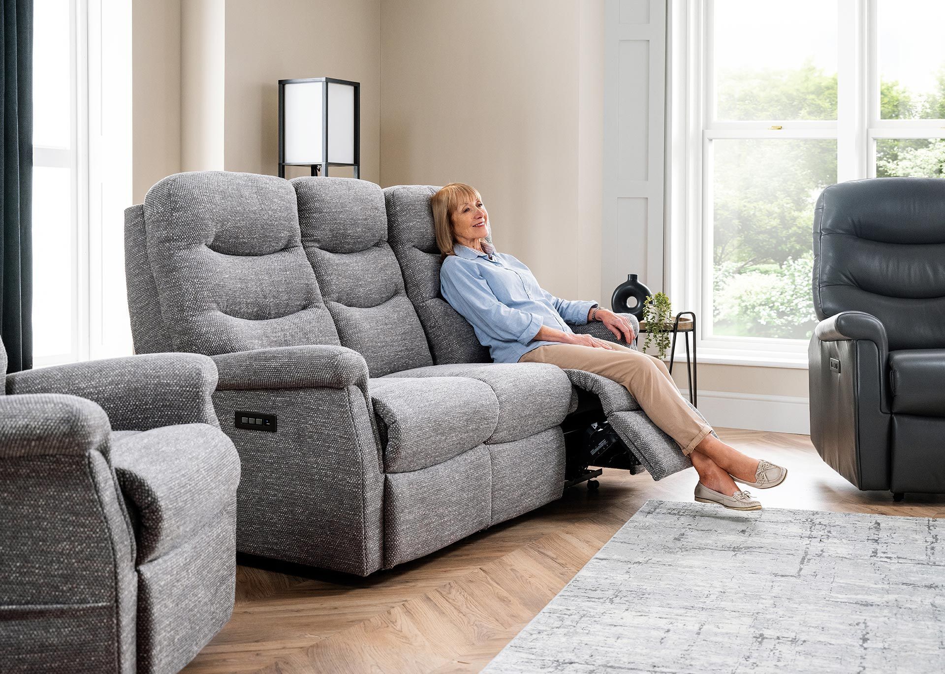 A woman relaxing on a gray recliner sofa in a bright living room,