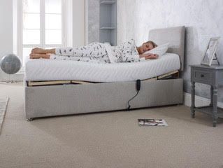 Person lying on a white bed in a bright bedroom beside a gray nightstand and window.