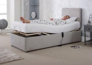Adjustable gray bed with raised mattress, person reclining in white bedding in a bright bedroom