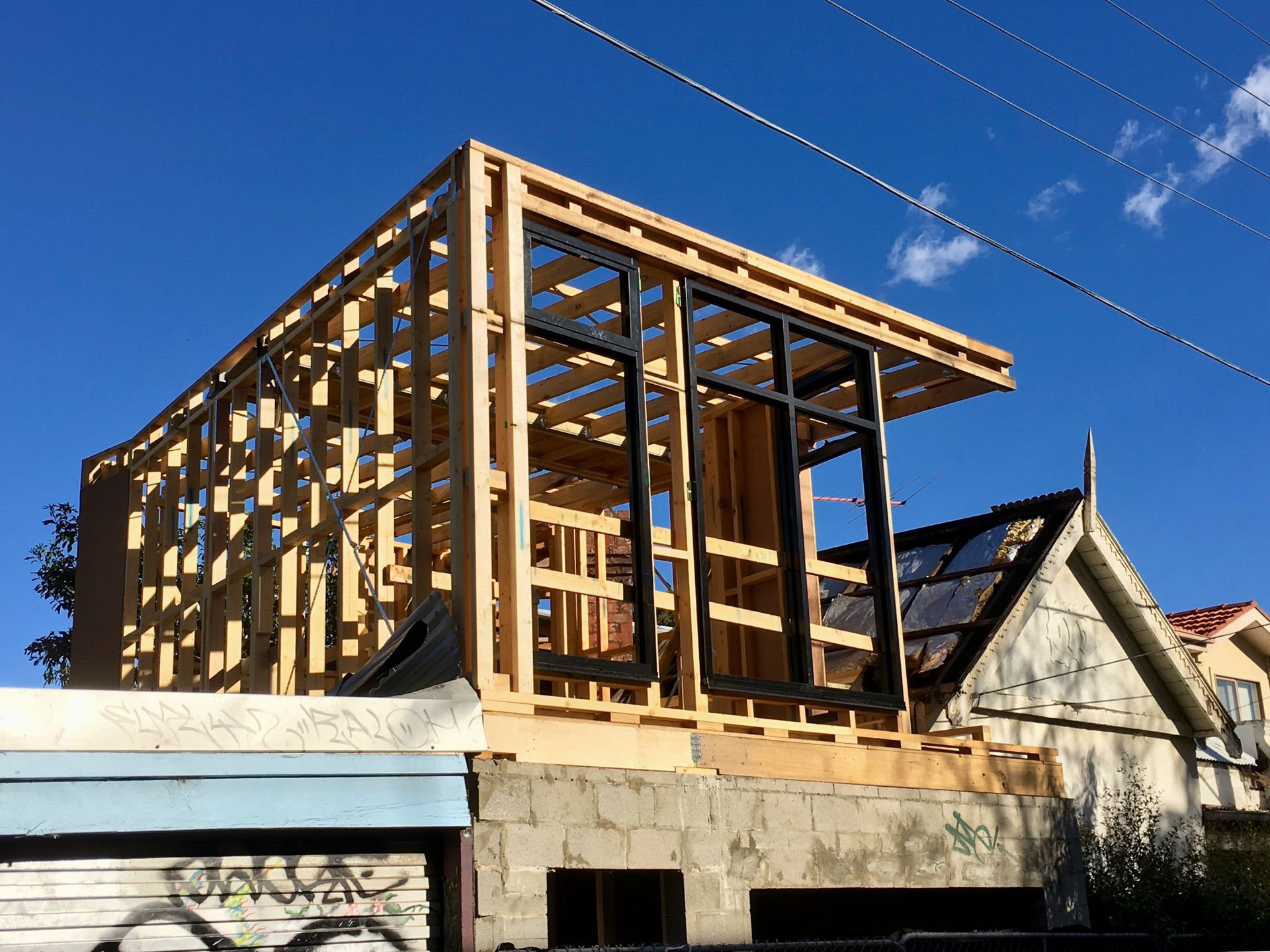 Une structure en bois en construction avec charpente apparente, grandes fenêtres noires, surplombant une base en béton, à côt