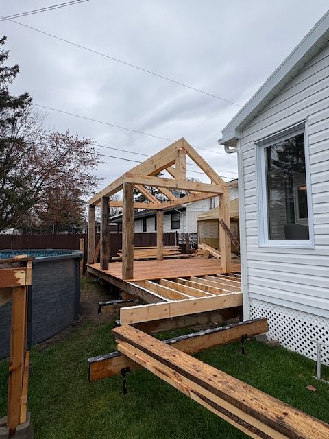Terrasse en bois en construction, avec une structure de toit de type gazebo, à côté d'une maison.