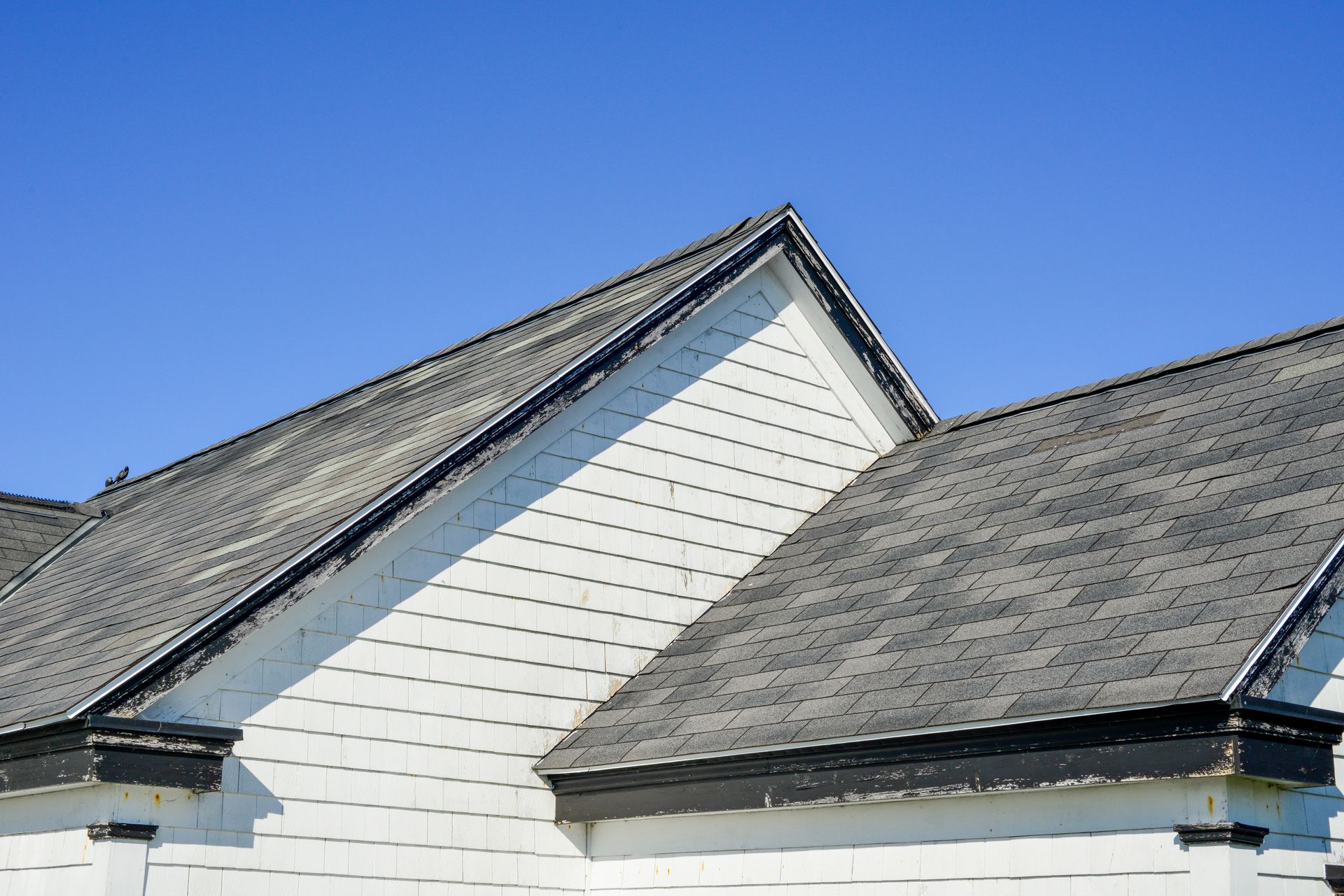 Détail de toiture avec bardeaux gris et pignons blancs sous ciel dégagé.