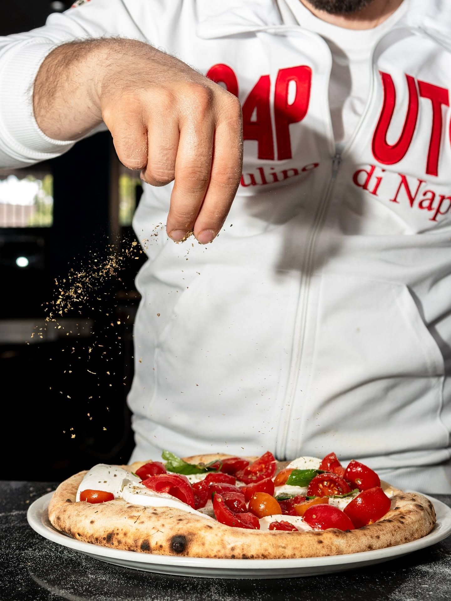 Chef che sparge condimento su una pizza Margherita in una teglia