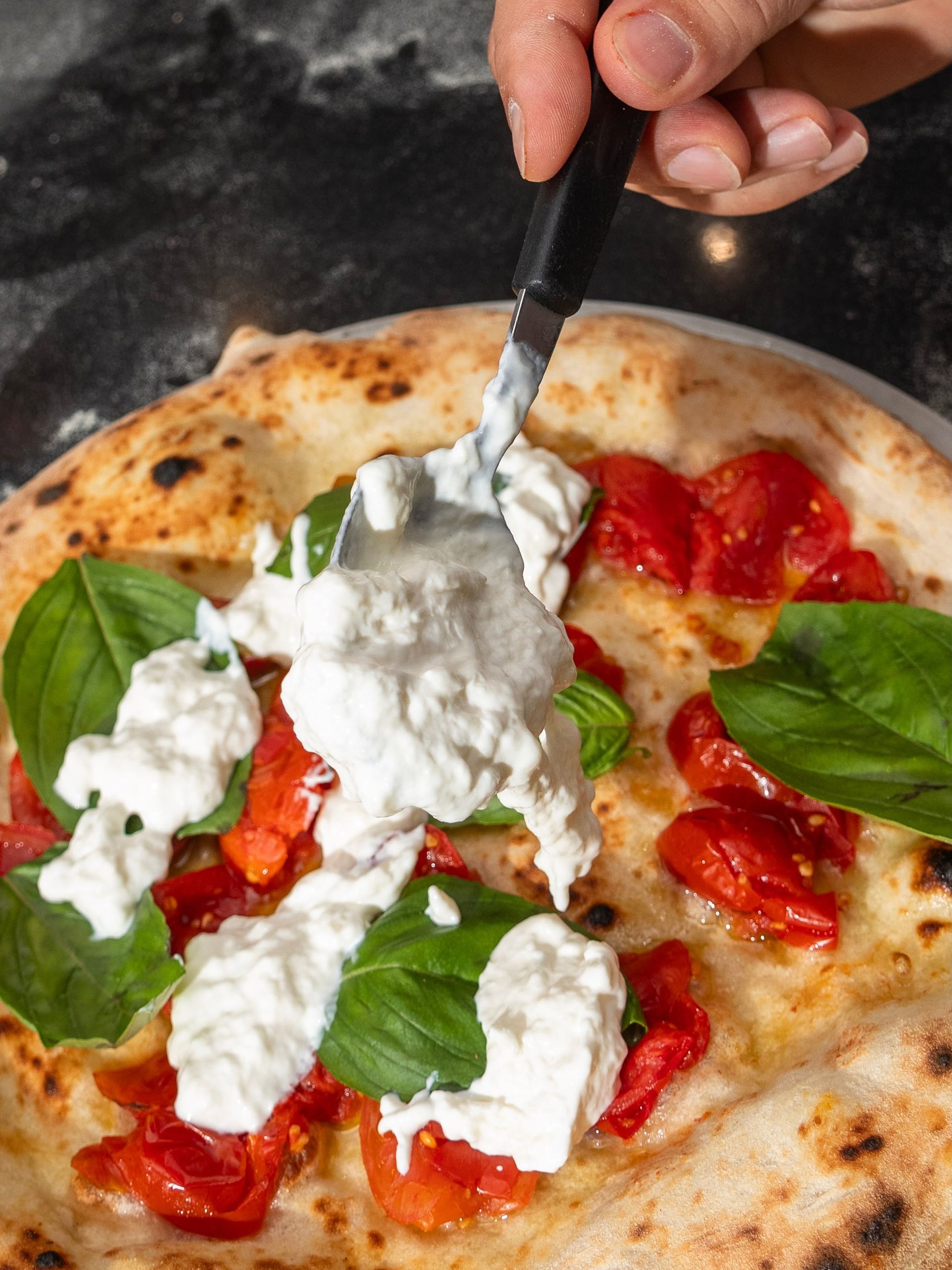Una mano che aggiunge a una pizza formaggio bianco, salsa rossa e foglie di basilico