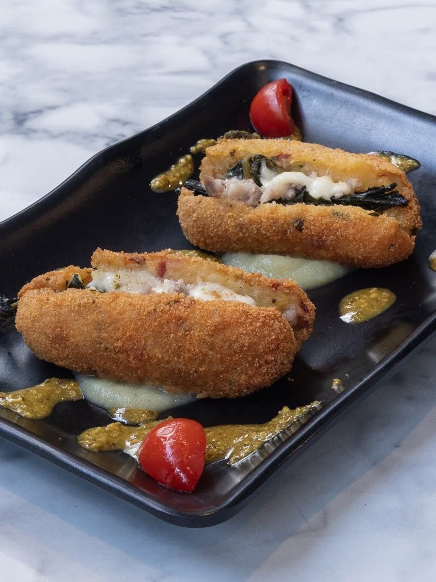 Tre crocchette fritte su un piatto nero con salsa e pomodorini ciliegia