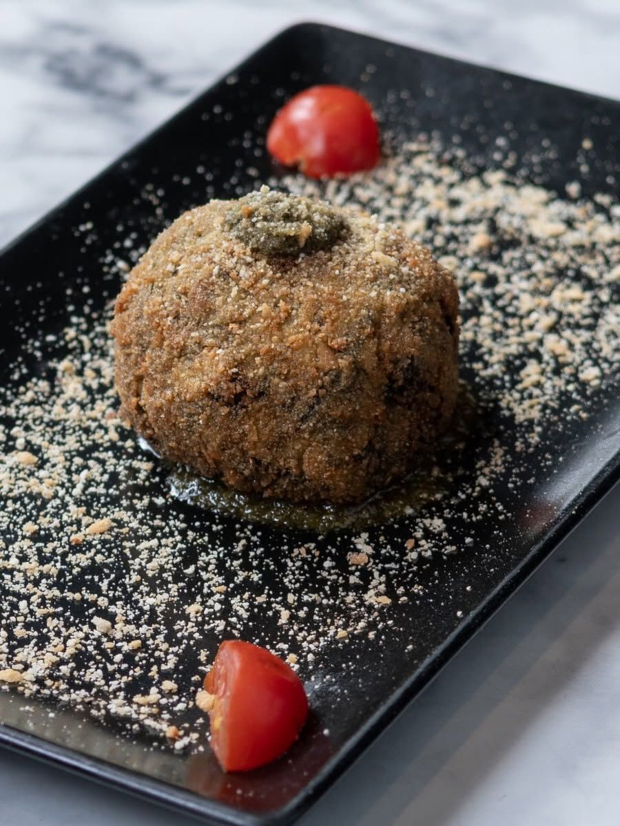 Dolce impanato su un piatto nero, spolverato di zucchero a velo e guarnito con fragole.