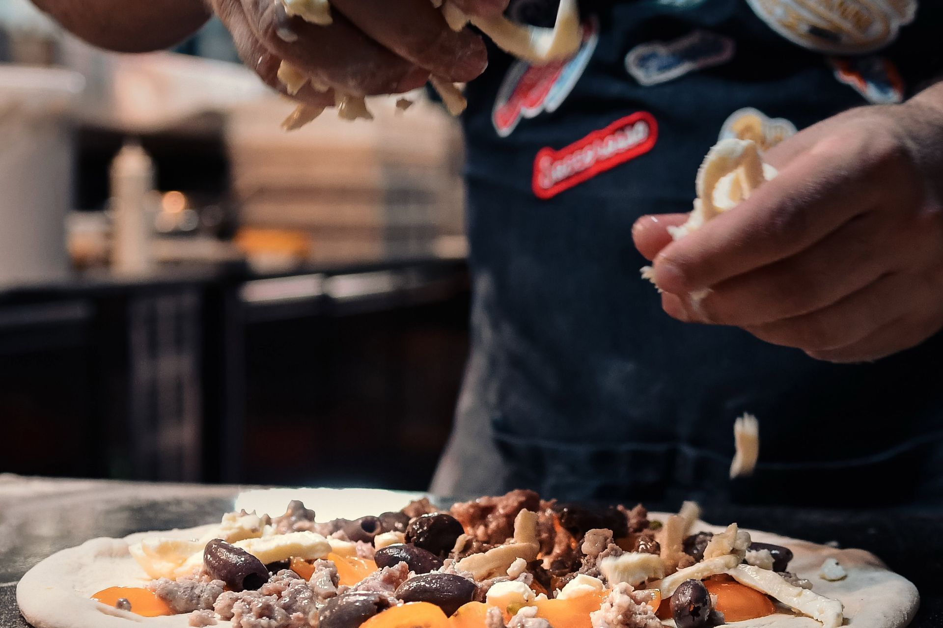 Mani che guarniscono una pizza con funghi e olive in una cucina attrezzata per la preparazione dei cibi