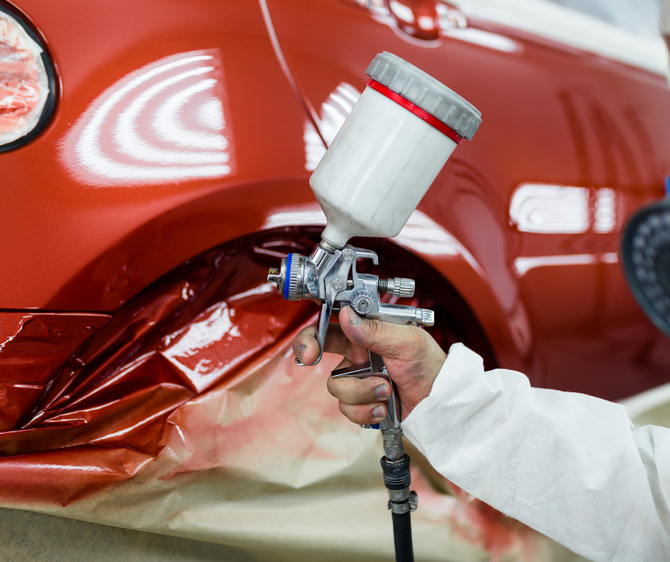 Hand spraying red paint on a car body in an auto shop