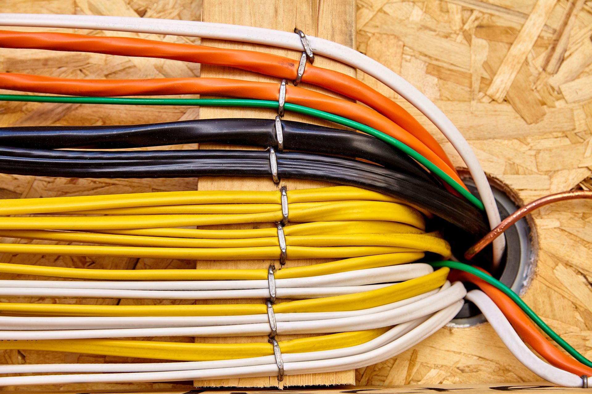 Bundles of colorful electrical cables routed through a wooden wall opening