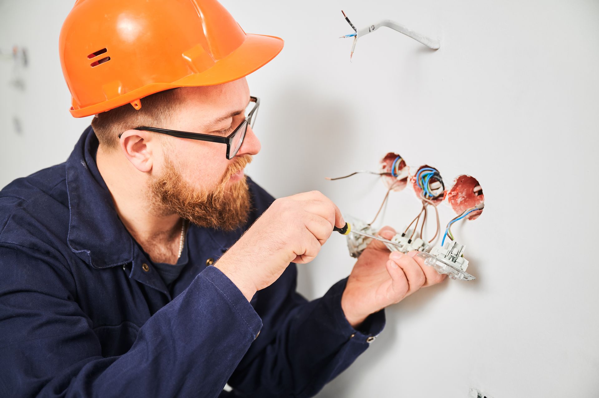Electrician in orange hard hat examining a wall wiring diagram while pointing at exposed wires