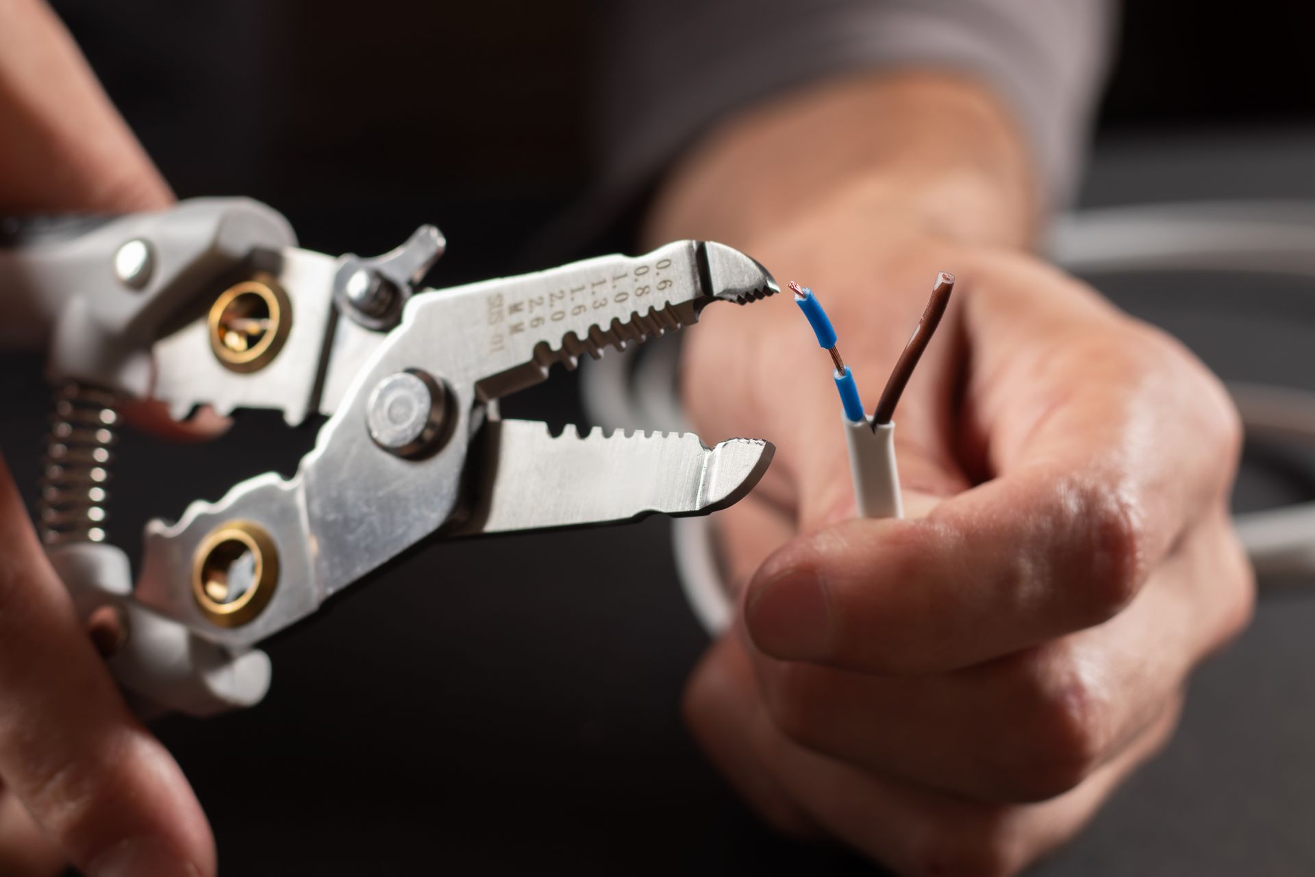 Hands using wire strippers to strip insulation from a black cable with blue and brown wires exposed