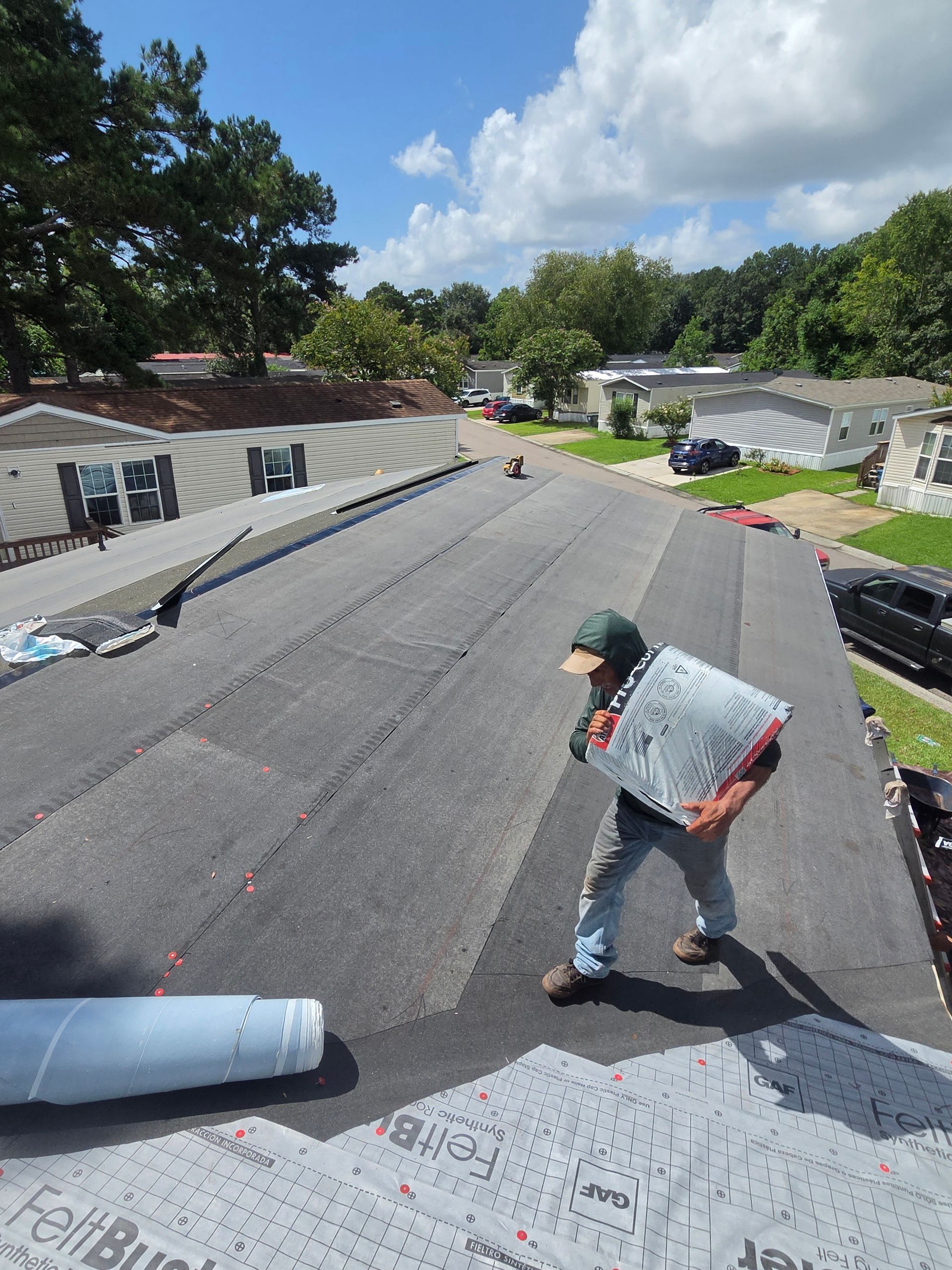 A Charleston Roofs and Windows crew installing a new Atlas architectural shingle roof on a raised, three-story oceanfront home on Isle of Palms, SC, with sea oats and dunes in the foreground and the Atlantic behind the house. A W2 project manager checks the ridge line from the elevated deck, representing the roofing company serving Isle of Palms SC for roof inspections, roof repairs, roof replacements, siding, windows and gutters, rated 4.9 stars on Google.
