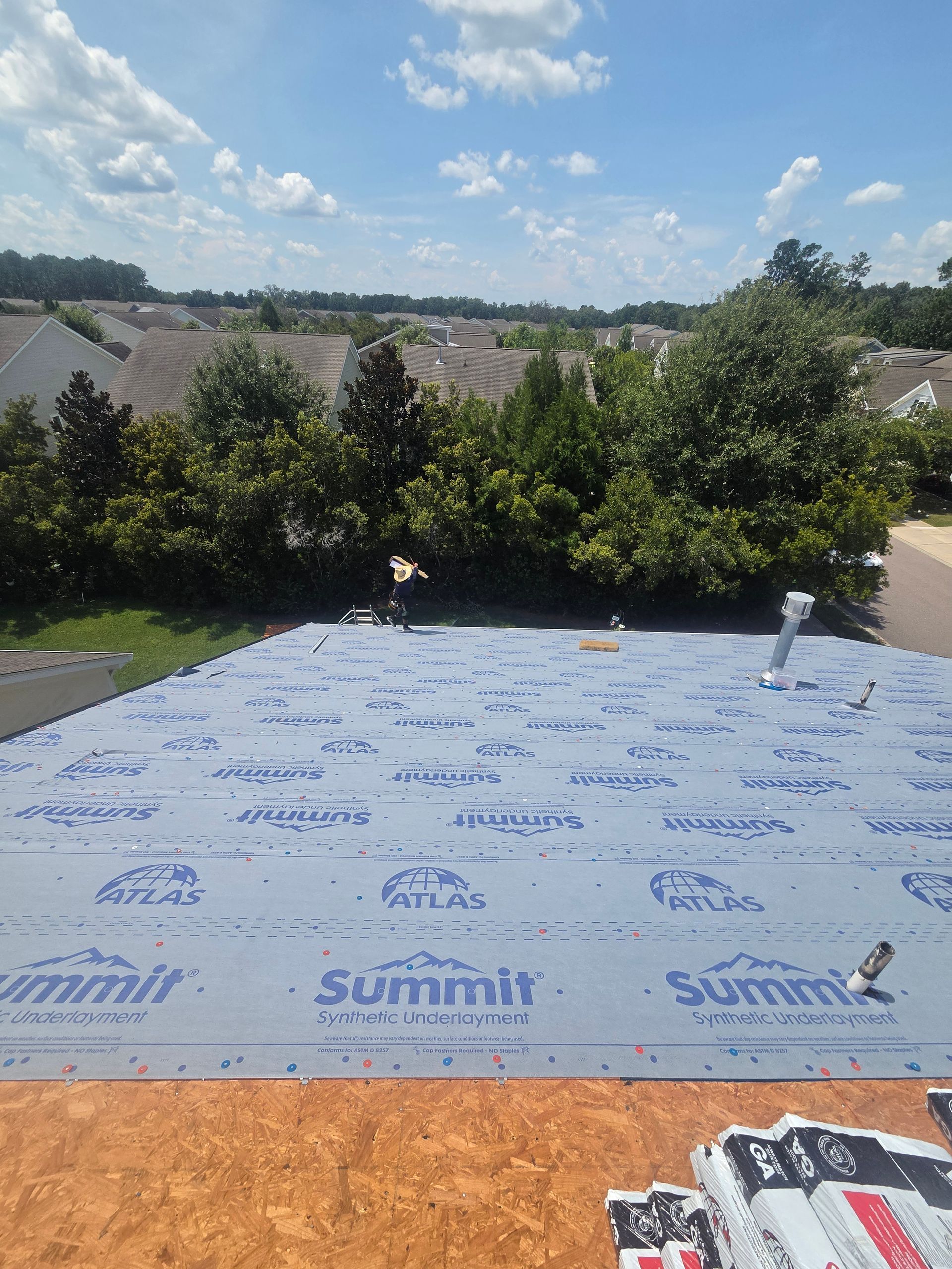 A Charleston Roofs and Windows crew finishing a new Atlas architectural shingle roof on a raised Seabrook Island, SC home facing the Bohicket Creek marsh, with new Viwinco windows, fiber cement siding and seamless gutters. A W2 project manager walks the roof with the homeowner under live oaks, showing the roofing company Seabrook Island homeowners call for inspections, repairs, replacements, siding, windows and gutters.