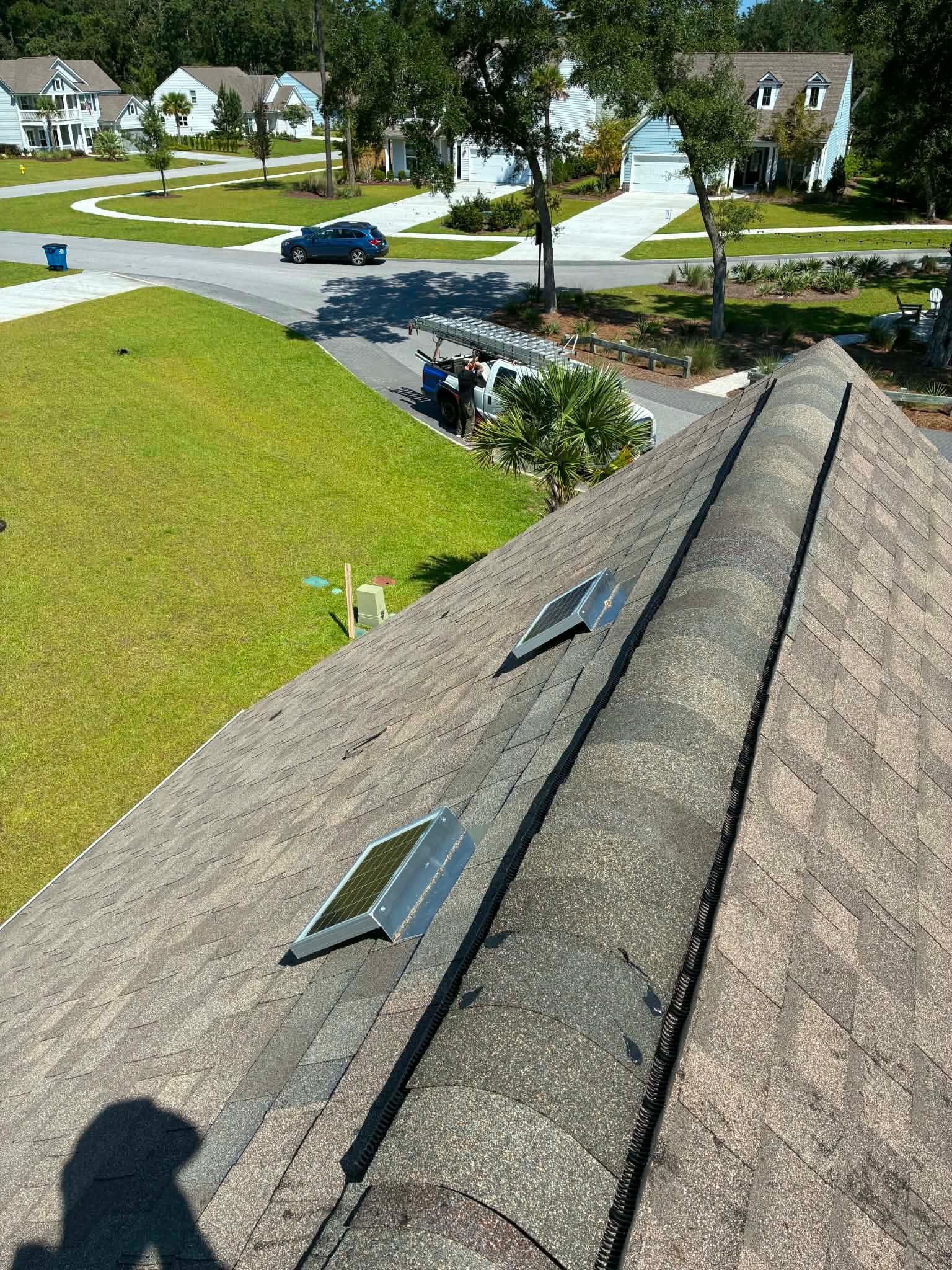 Charleston Roofs and Windows inspection manager Eric Chesnutt on a ladder photographing flashing on a Charleston home while a homeowner watches from the yard. The image shows the free roof inspection that starts every Charleston Roofs and Windows project, covering roof repairs, emergency roof repairs, full roof replacements and storm damage from wind, hail and hurricanes, backed by a locally owned company founded in January 2012.