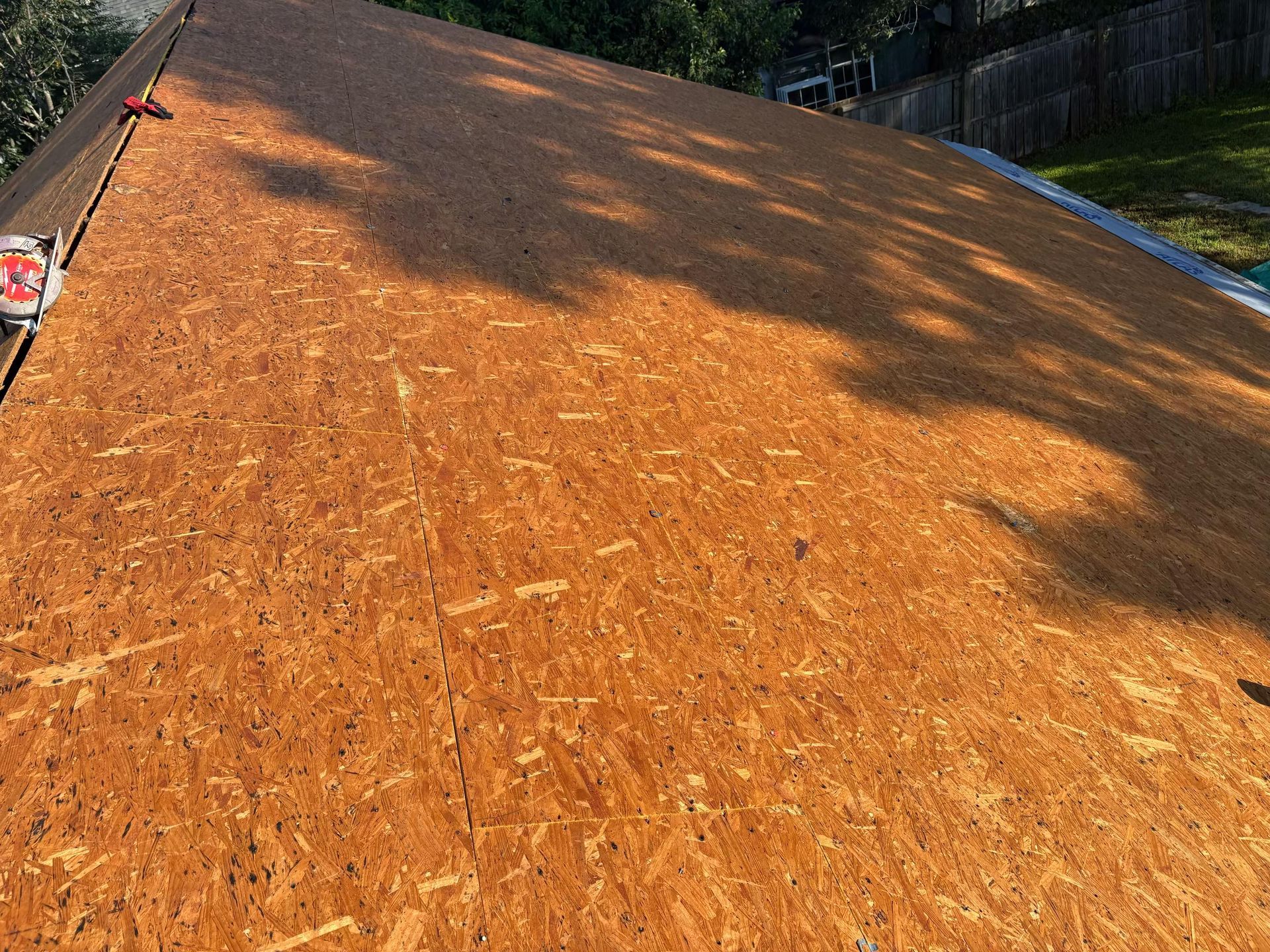 A Charleston Roofs and Windows inspection manager reviewing a line-item roof replacement estimate with a Goose Creek, SC couple at their front door, with pine trees and a half-finished Atlas shingle roof overhead. The image represents roof replacement cost in Goose Creek, priced per square for asphalt shingles, metal and flat roofs, with free inspections, veteran specials and 0% financing for 12 months on approved credit.