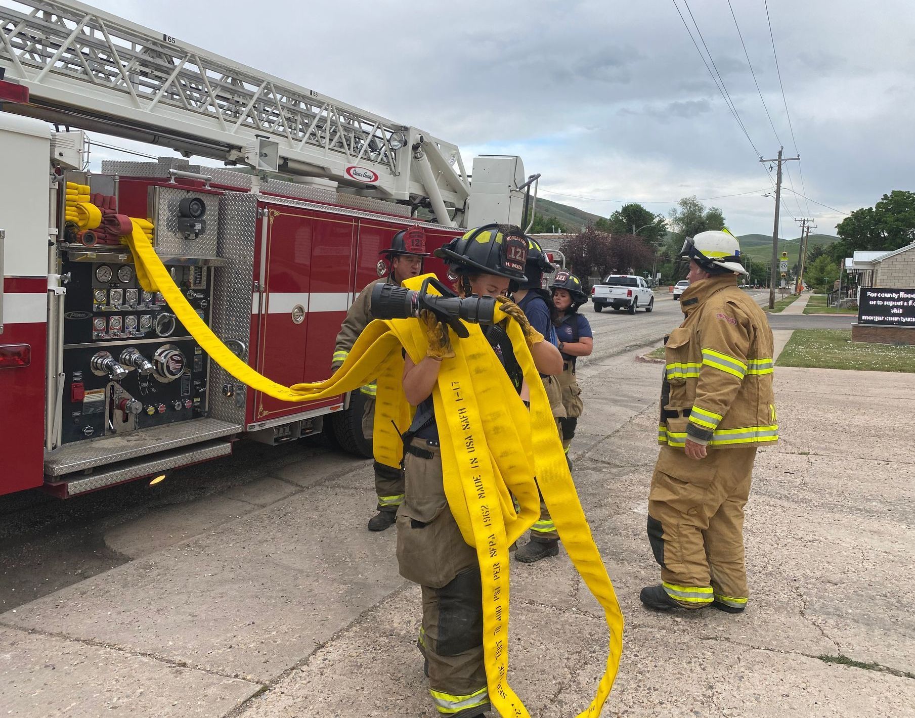 Firefighters preparing a yellow hose near a red fire truck.
