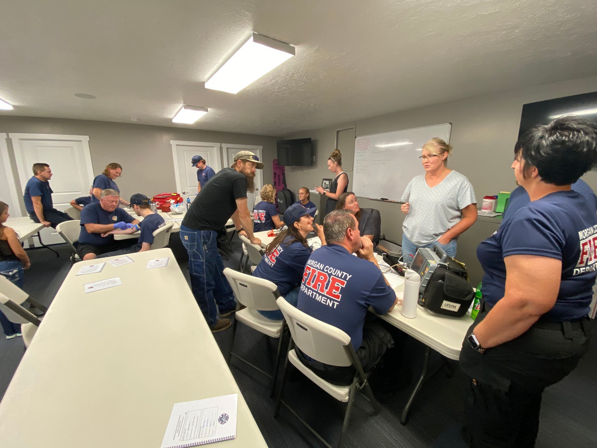 Firefighters in a room, some seated at tables, others standing and interacting.