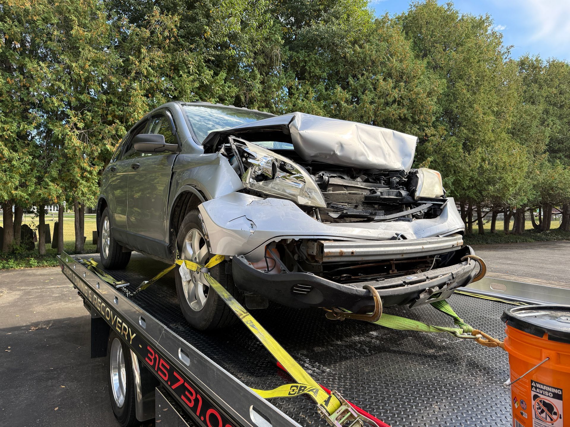 A damaged silver car sits on a flatbed tow truck with its front end heavily crumpled.