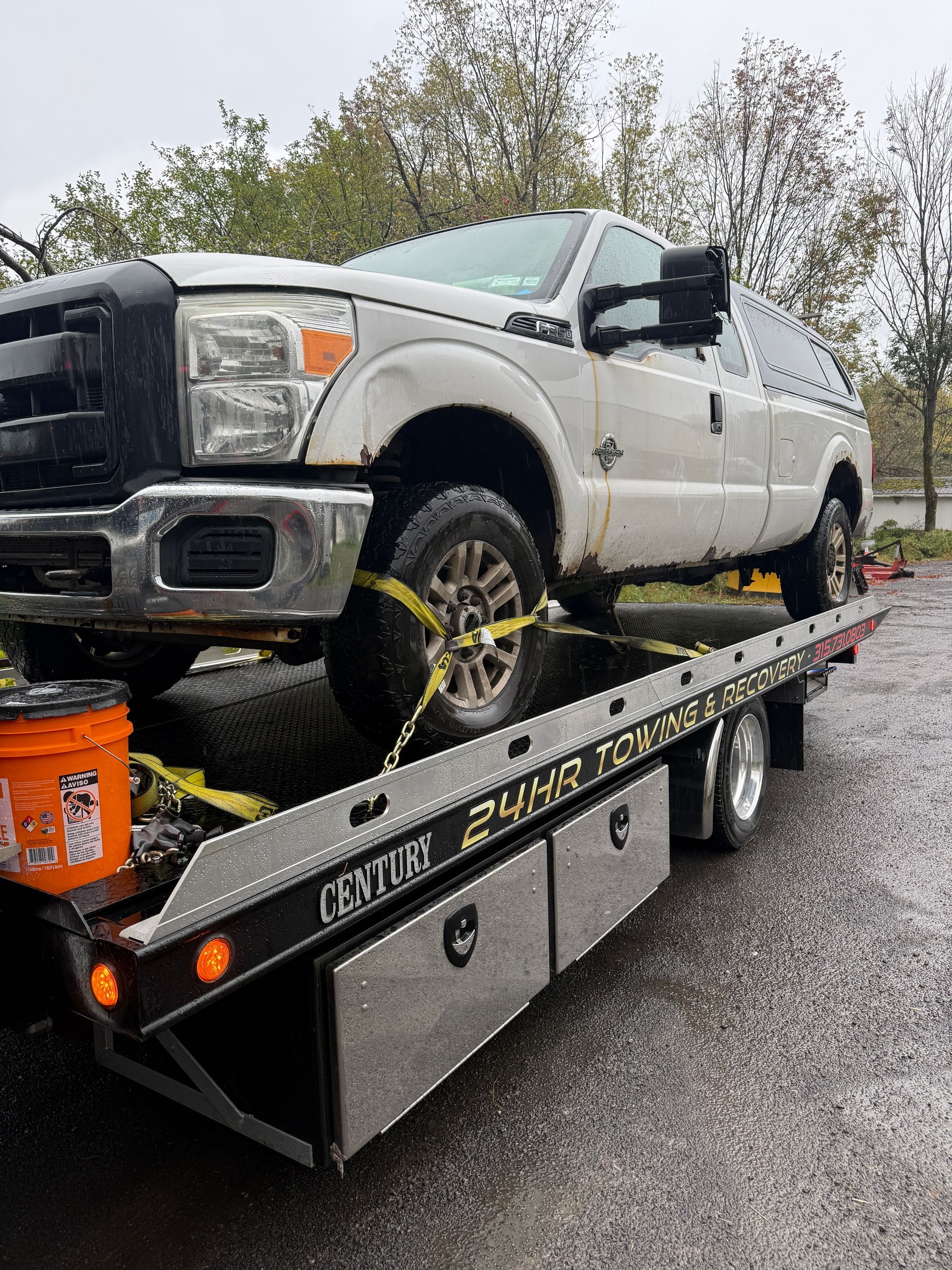 A white Ford pickup truck secured with yellow straps on a flatbed tow truck outdoors.
