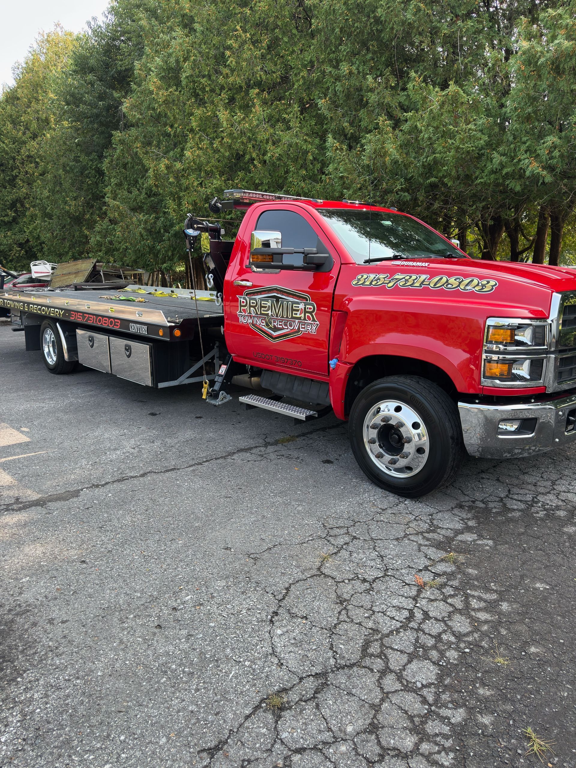A bright red flatbed tow truck parked on an asphalt lot in front of trees.