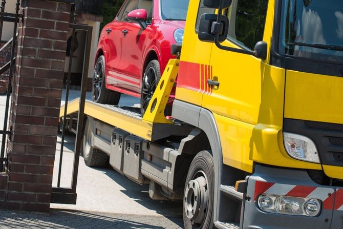 Red car on a yellow tow truck beside a brick building