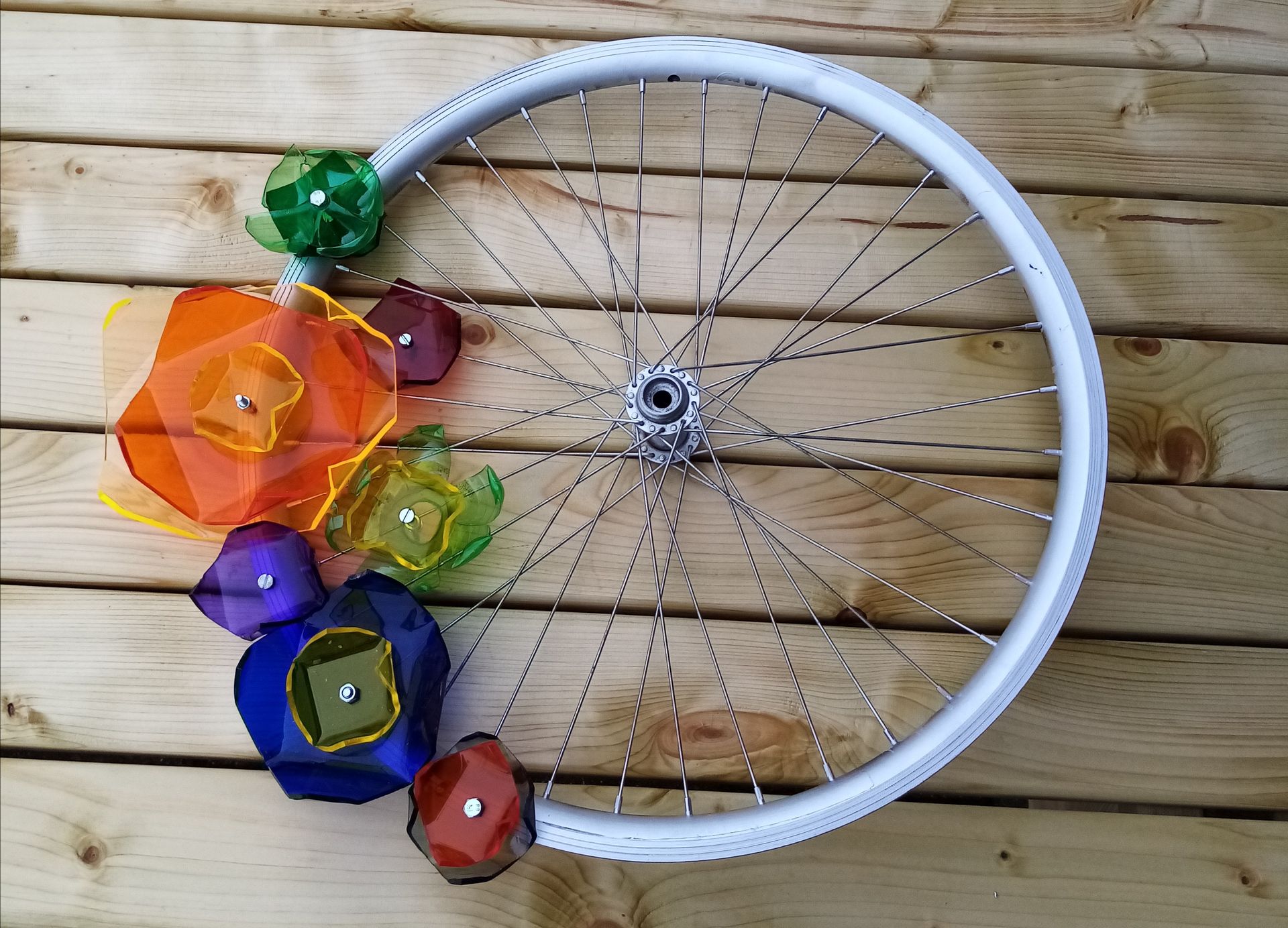 Een fietswiel versierd met kunststof bloemen. In de zon geeft deze mooie kleurige weerspiegelingen op de muur.
