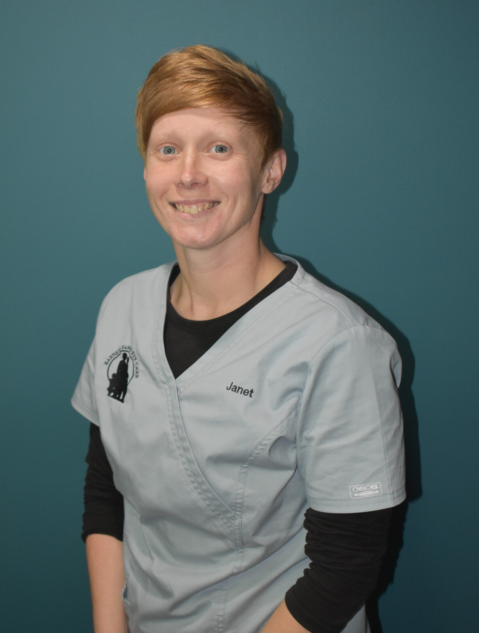 Smiling person in gray medical scrubs against a teal background
