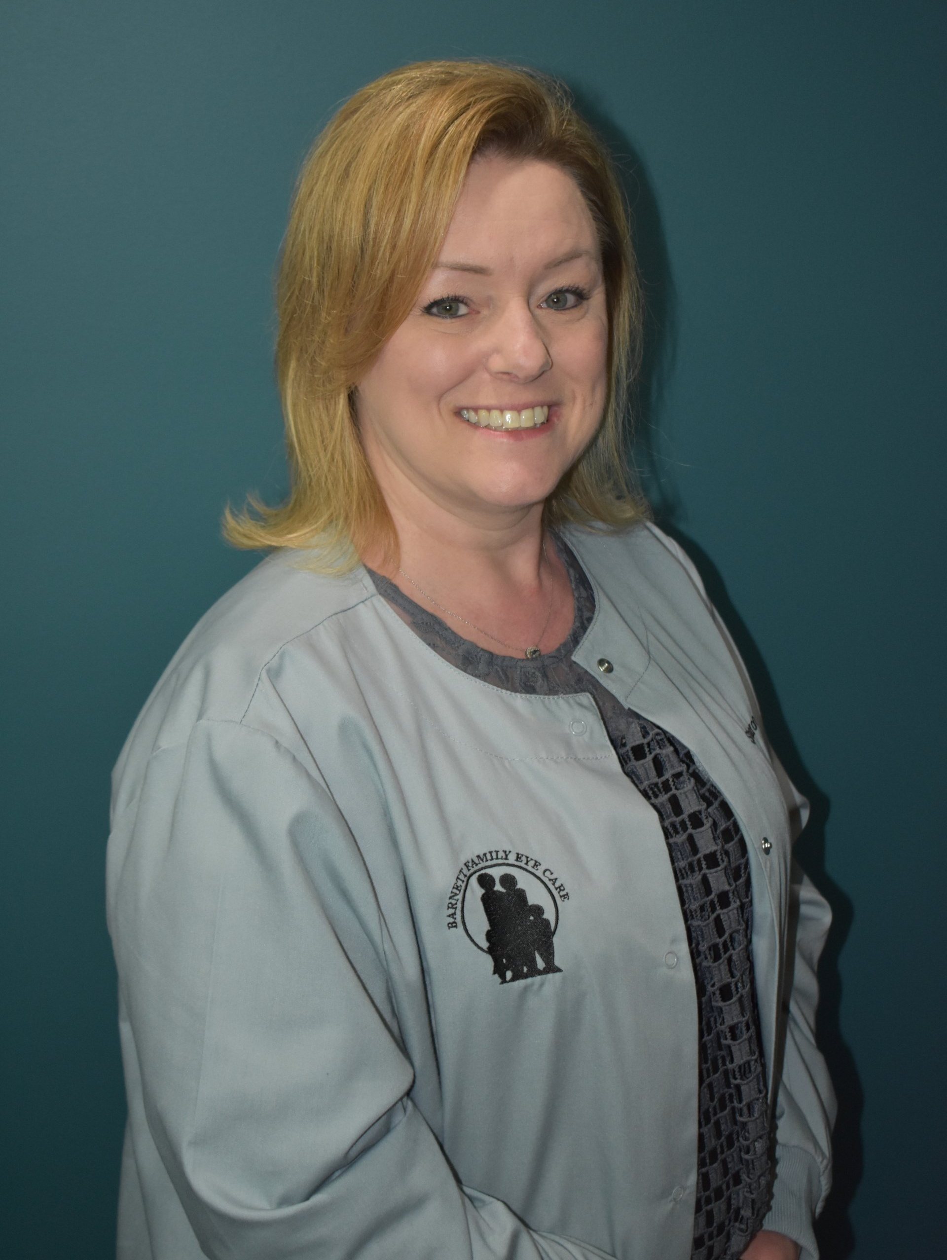 Woman smiling in a light gray jacket against a teal background