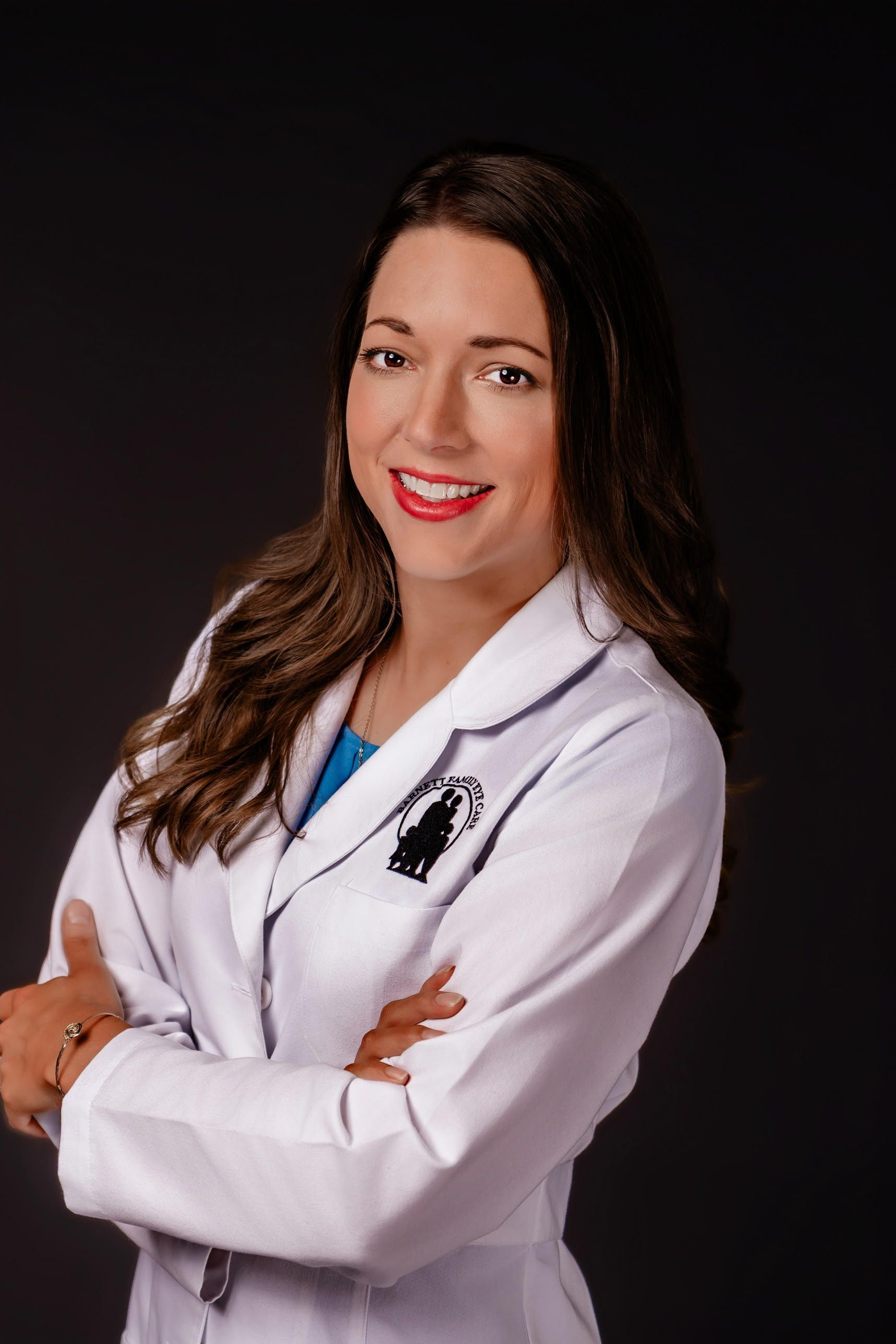Woman in a white lab coat smiling with arms crossed against a dark background