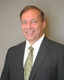 Smiling man in a dark suit with a green tie against a gray background