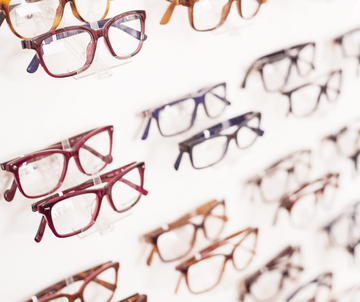 Assorted eyeglasses displayed on a white wall, in red, black, and brown frames