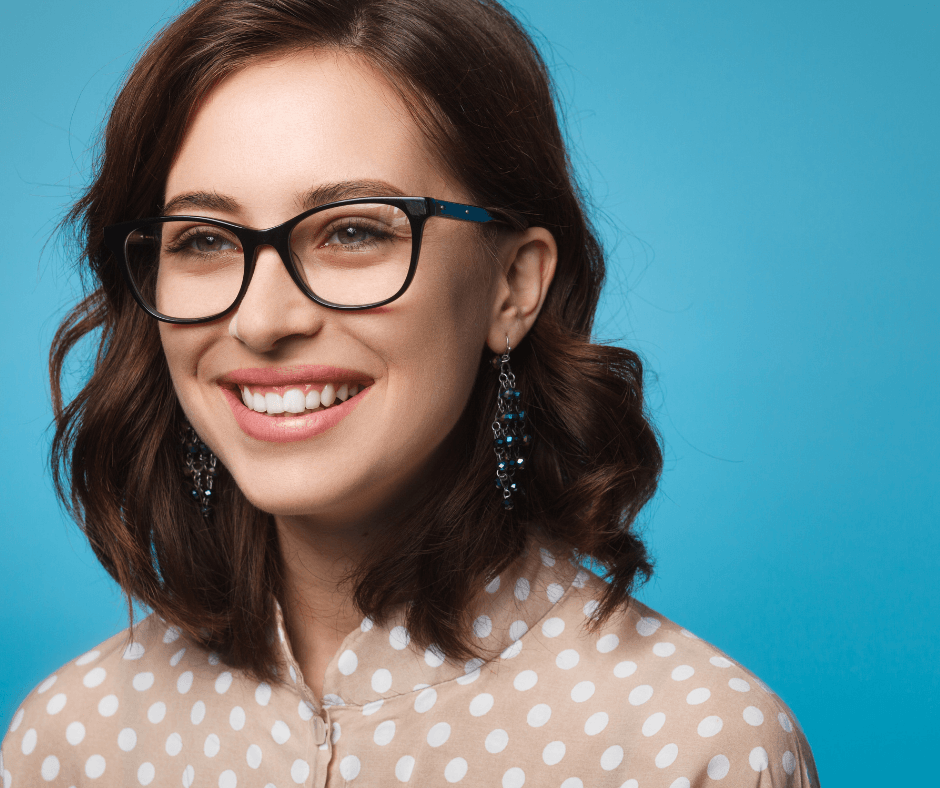 Smiling person wearing glasses and a white polka-dot top against a blue background