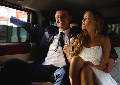 A bride and groom are sitting in the back seat of a limousine.