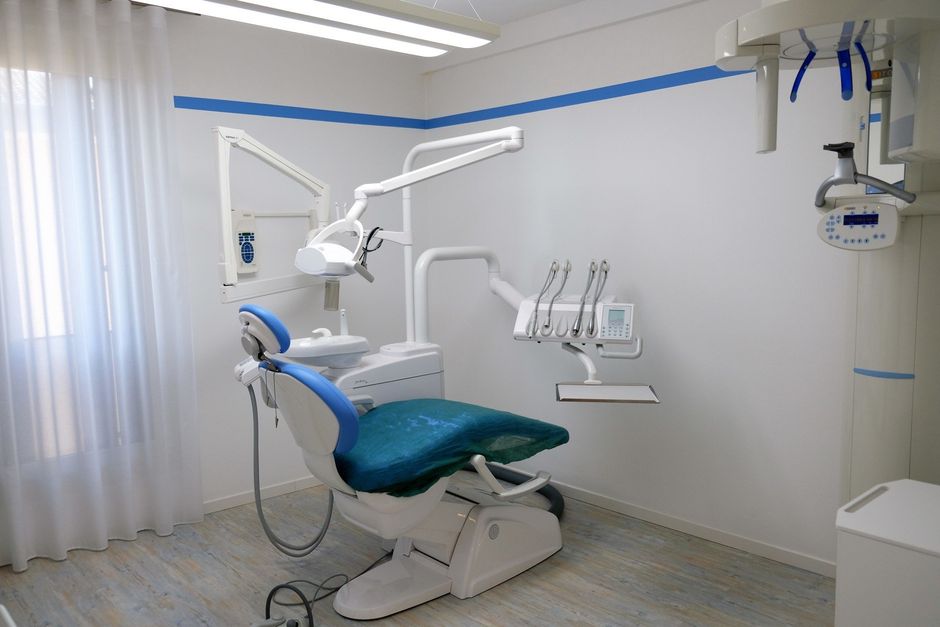 Poltrona odontoiatrica in una stanza bianca con dettagli e attrezzature blu.