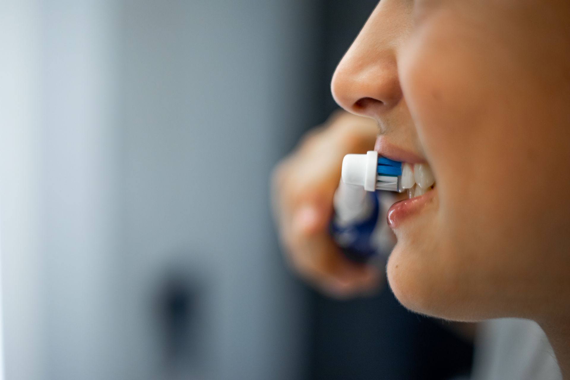 Persona che si lava i denti con uno spazzolino elettrico. Primo piano, vista laterale in un bagno.