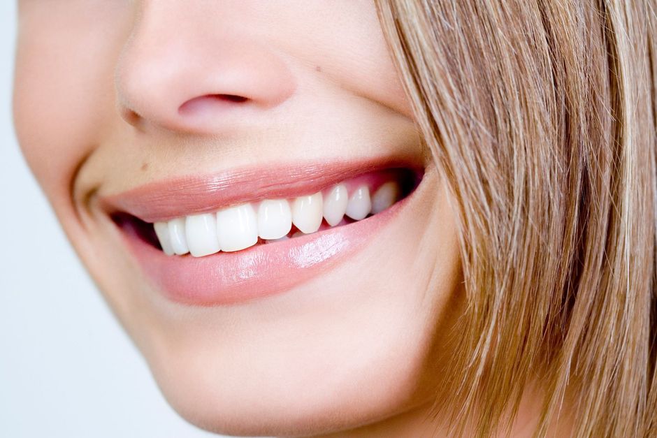 Primo piano di una bocca sorridente con denti bianchi e brillanti e labbra rosa e lucide.