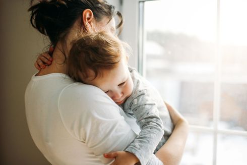 A woman is holding a baby in her arms in front of a window.
