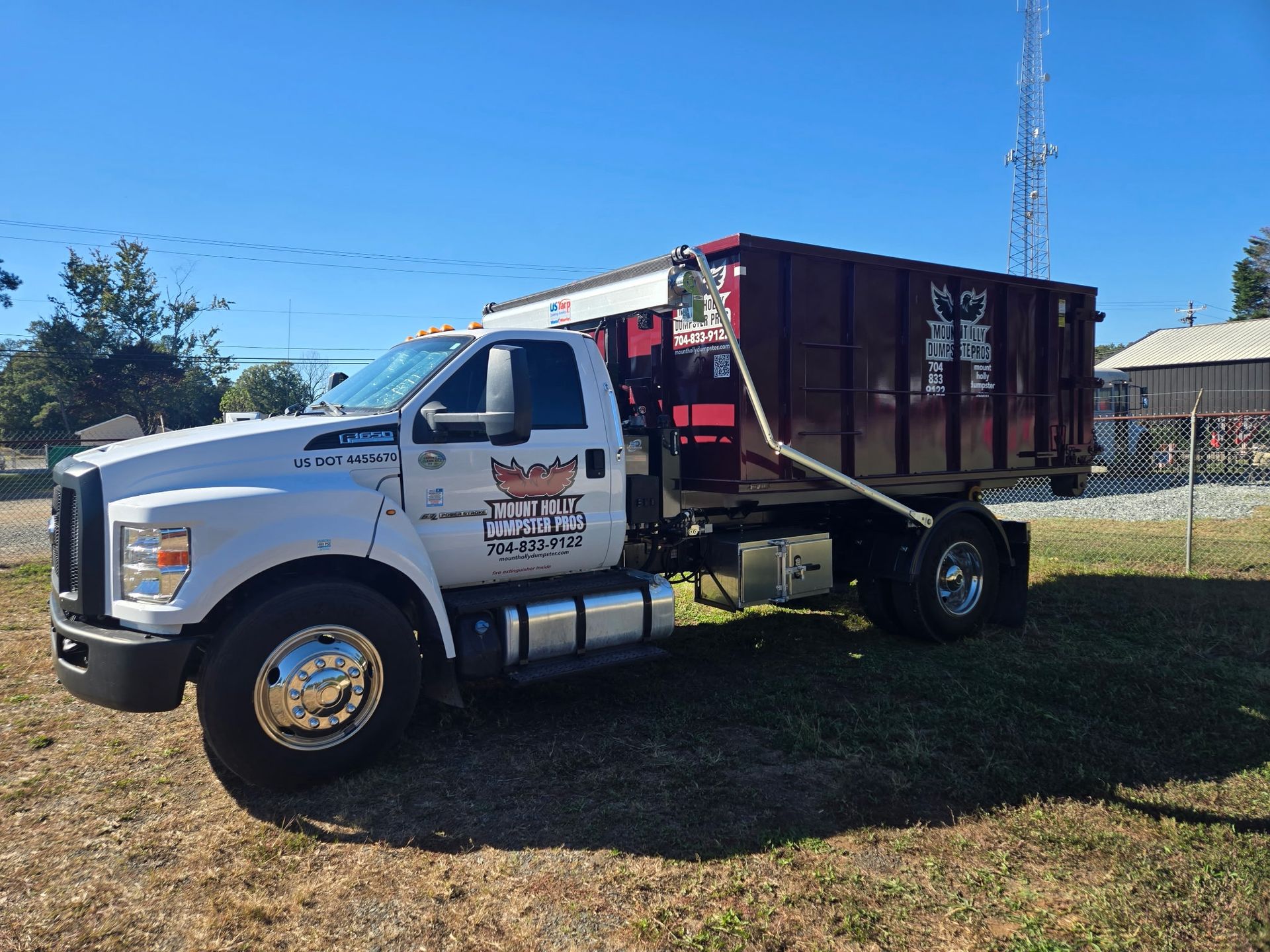 White dump truck with maroon bed parked on grass under a clear blue sky.