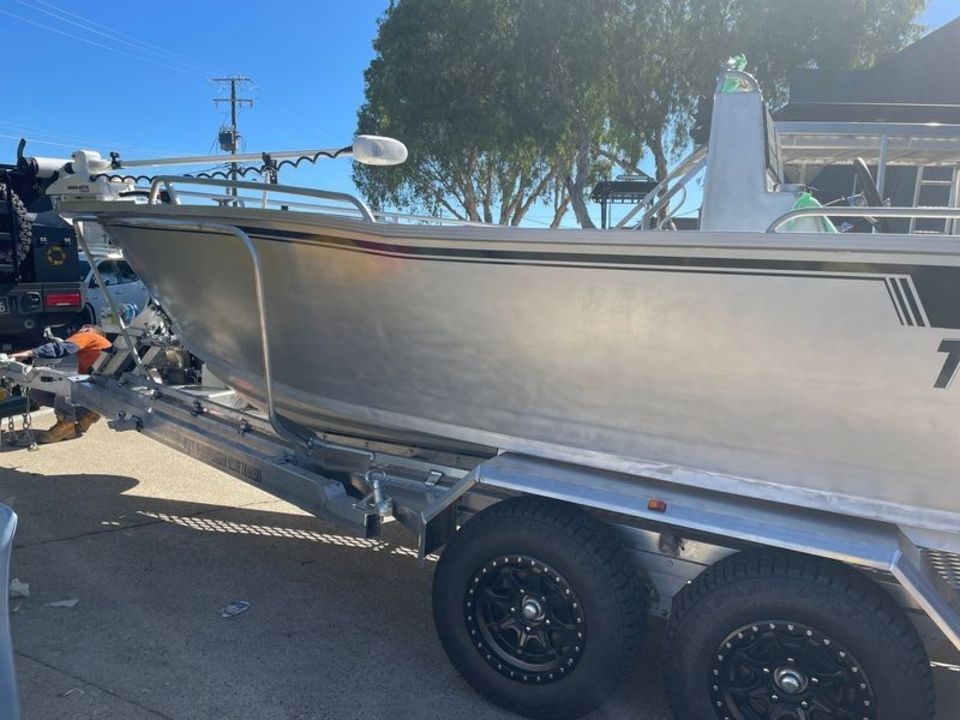 A silver boat is on a trailer in a parking lot.