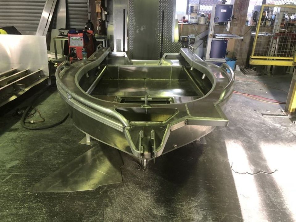 A stainless steel boat is sitting on the floor in a factory.