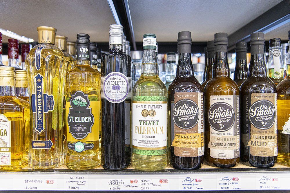 Bottles of various liquor brands on a shelf in a store, lit from above.