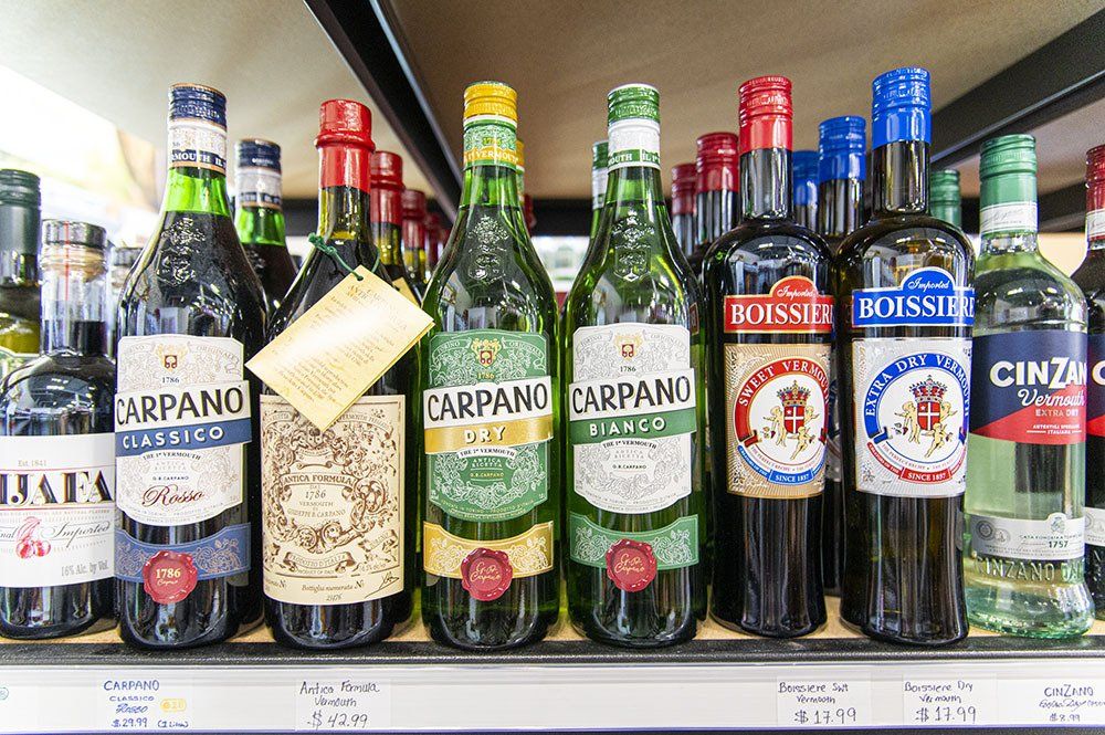 Bottles of Italian vermouth and other liquors on a store shelf, various labels and colors.