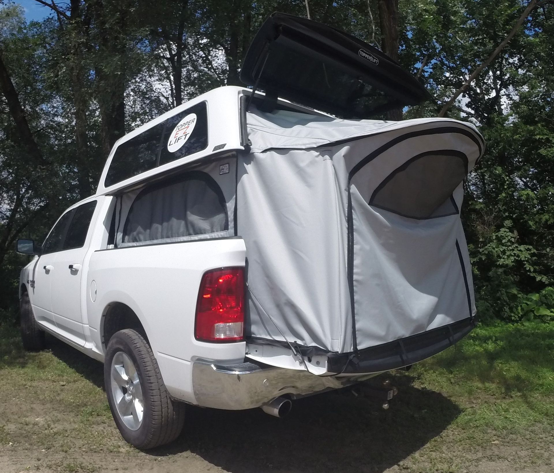 White pickup truck with a Topper EZ Lift camper shell and tent extension in a wooded area.