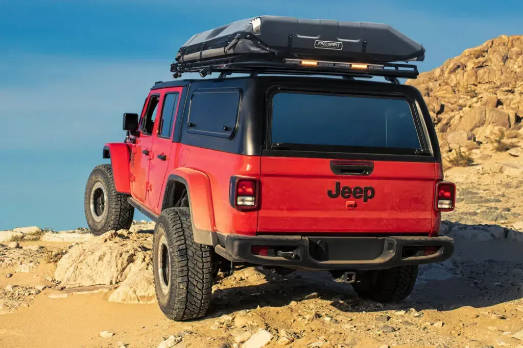 Red Jeep Gladiator with black roof, on a rocky terrain, with roof-mounted tent.
